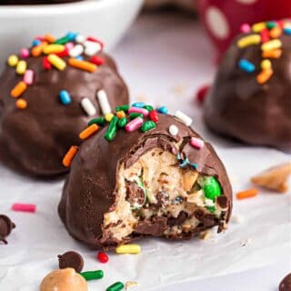Cookie dough truffles dipped in chocolate with sprinkles on parchment paper.