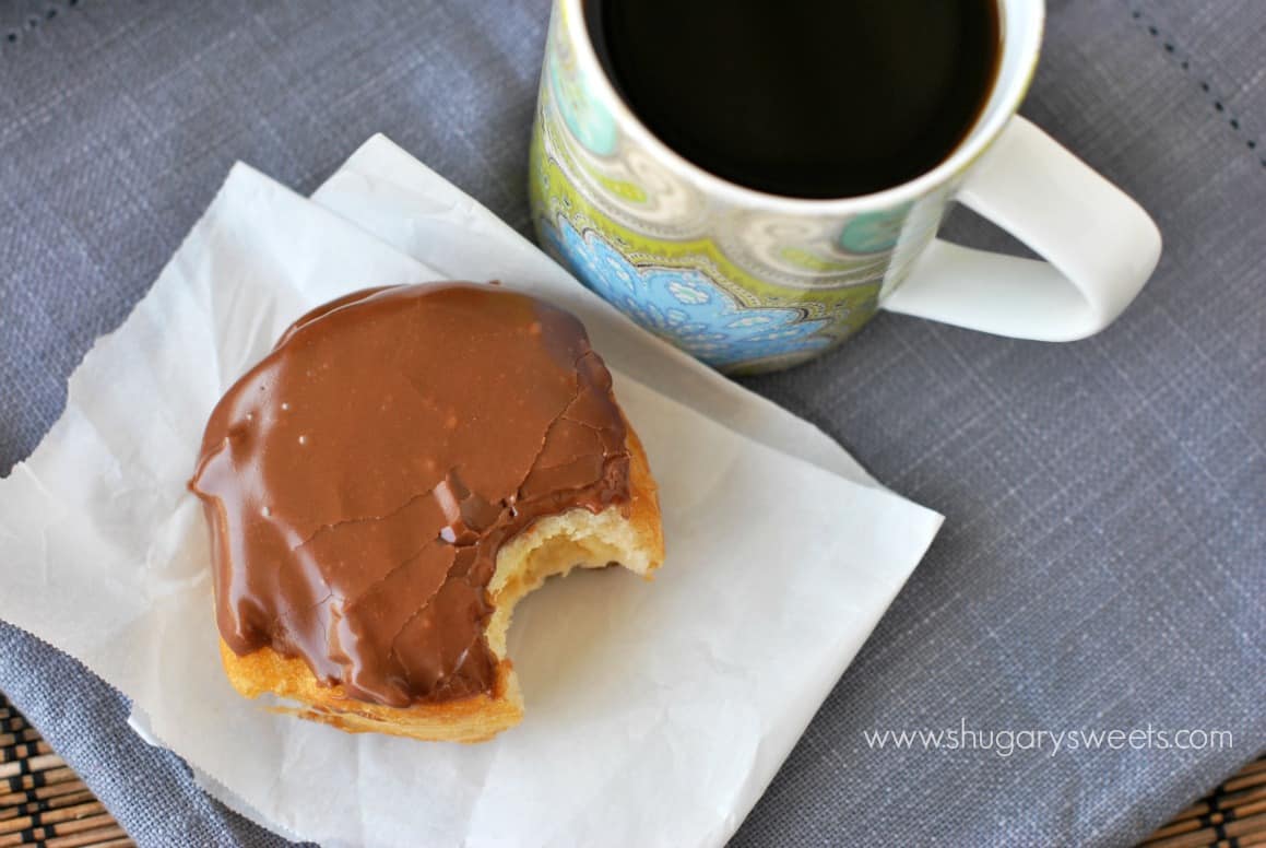 Boston Cream Donuts with a bite taken out of it, and a mug of black coffee.