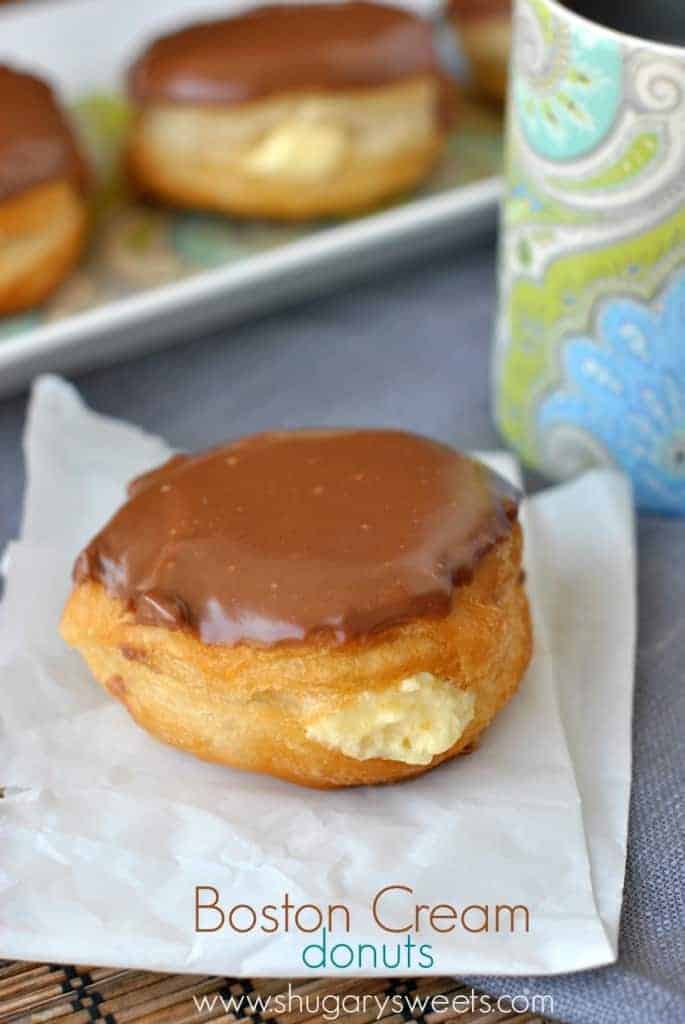 Boston Cream Donuts: easy, fast, delicious with Pillsbury Grands, pudding mix and chocolate ganache! Boston Cream Donuts on a piece of parchment paper with a mug of coffee.