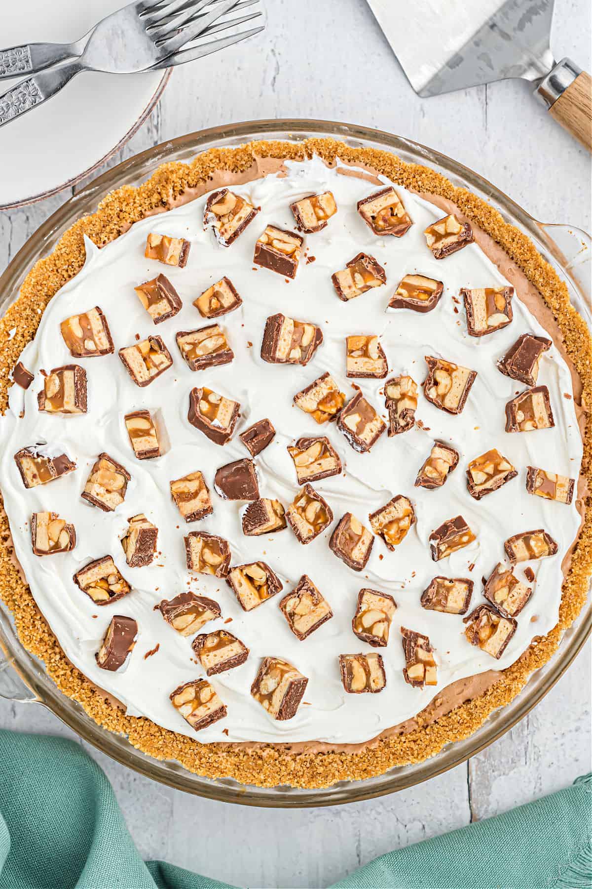 Snickers pie garnished with cool whip and chopped candy bars in a pie plate.