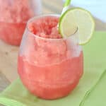 Watermelon slush in stemless wine glass with lime slice garnish.