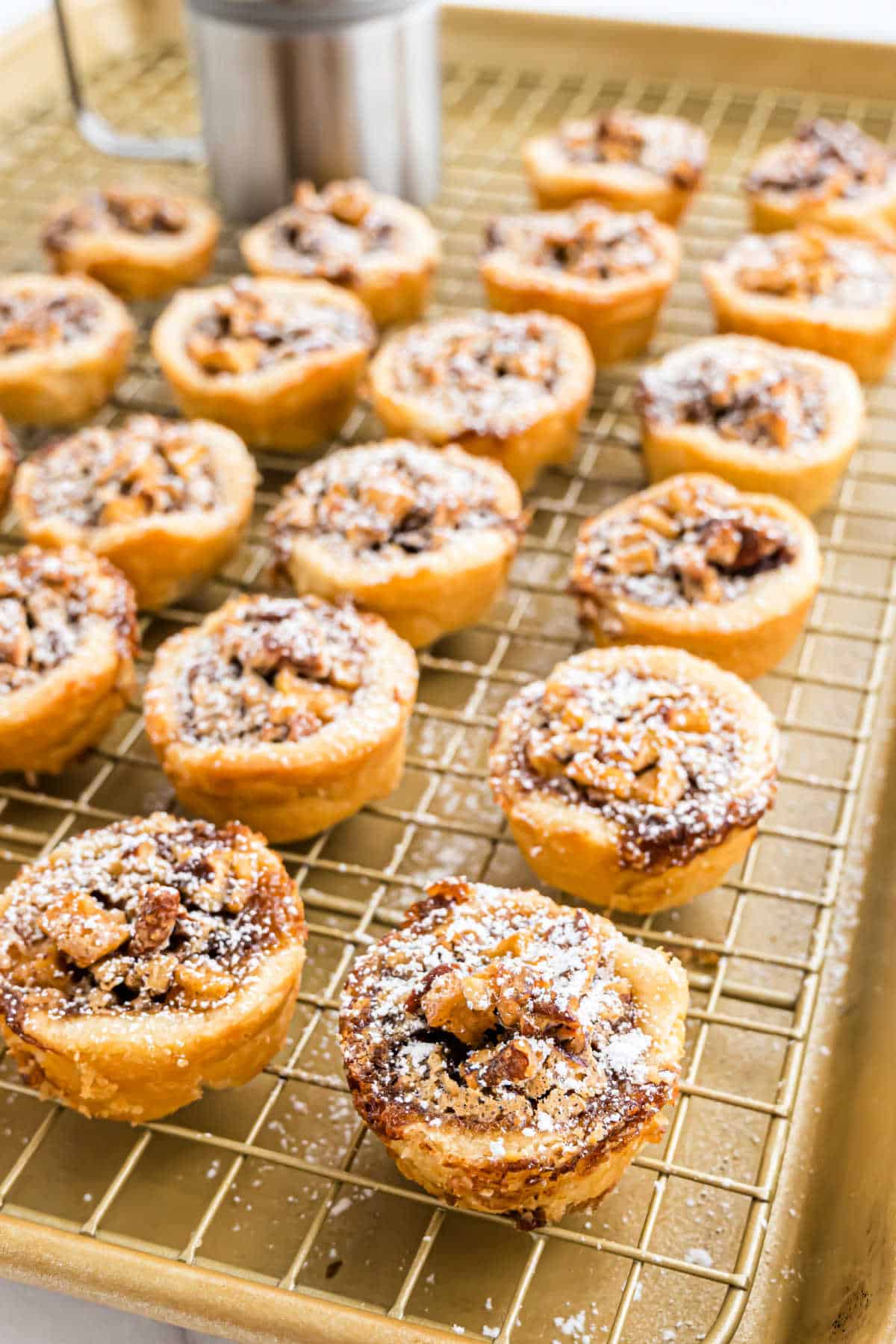 Mini apple pecan cups dusted with powdered sugar cool on a rack set over a baking sheet.