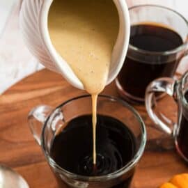 Pumpkin coffee creamer being poured into a mug of hot, black coffee.