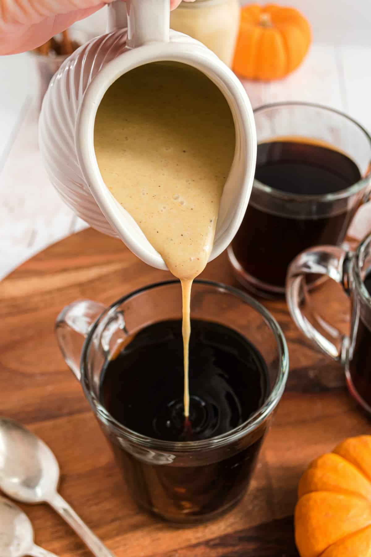 Pumpkin coffee creamer being poured into a mug of hot, black coffee.