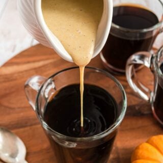 Pumpkin spice creamer being poured into mug of black coffee.