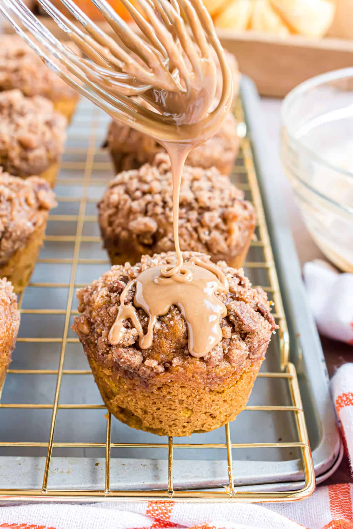Pumpkin muffins on wire rack with maple icing being drizzled over the top.
