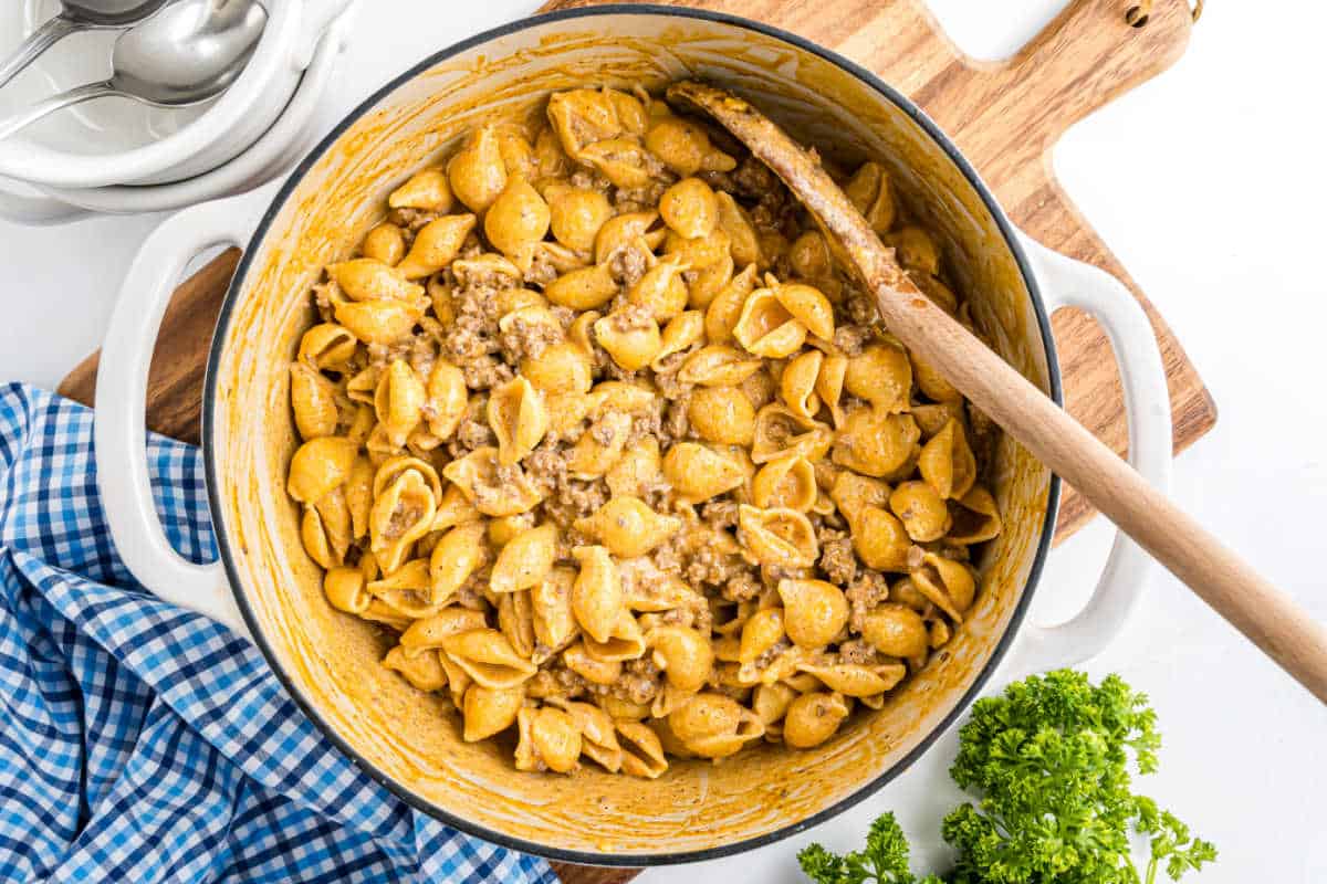 Shell pasta with ground beef and creamy sauce in a white pot, stirred with a wooden spoon—like a comforting beef enchilada mac and cheese perfect for family dinners.