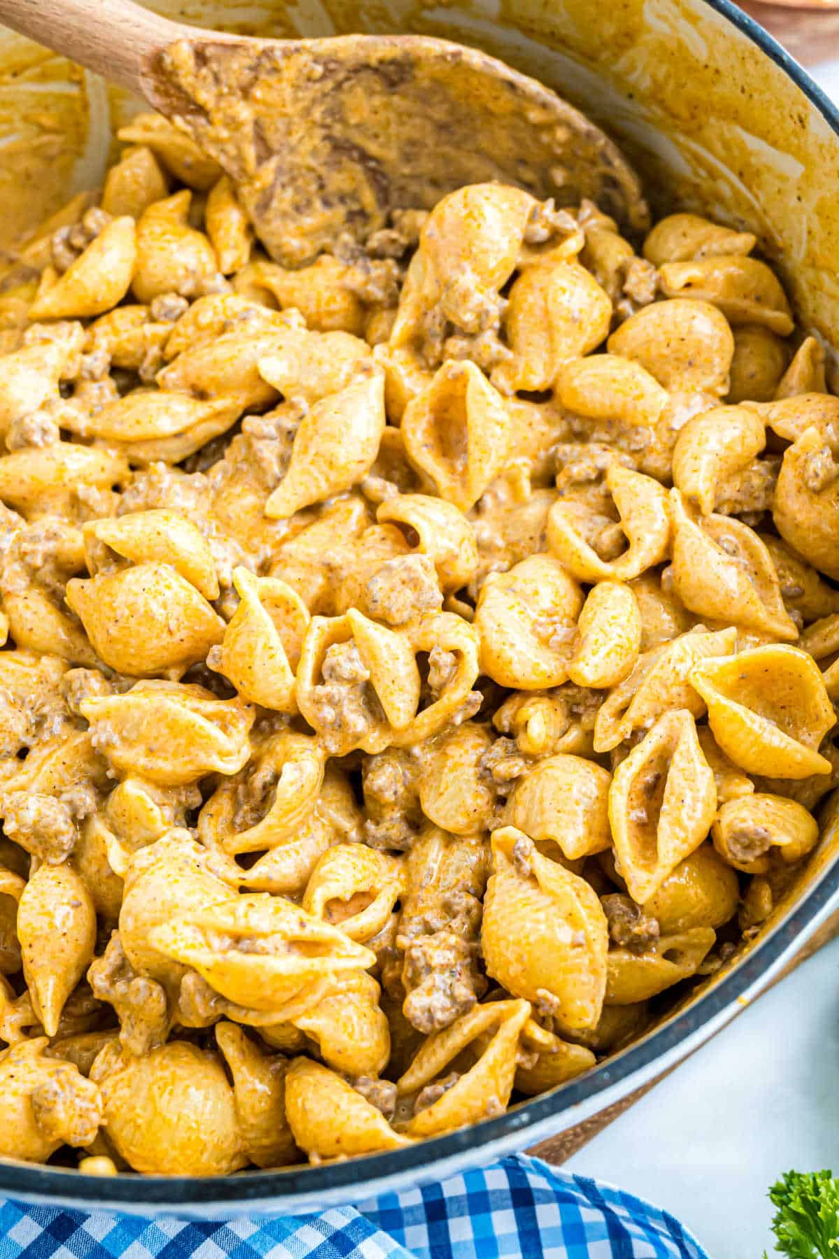 Shell pasta mixed with creamy, cheesy sauce and ground beef enchilada mac and cheese, being stirred with a wooden spoon.