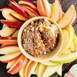 Apple dip with caramel and cream cheese in a bowl surrounded by sliced apples.