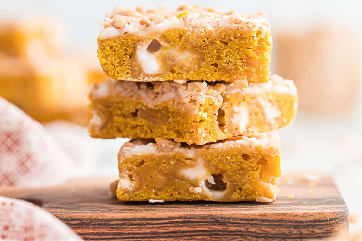 Stack of three pumpkin iced blondies on wooden cutting board.