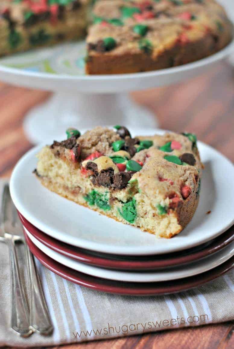 Slice of coffee cake with red and green chocolate chips on a stack of red and white dessert plates.
