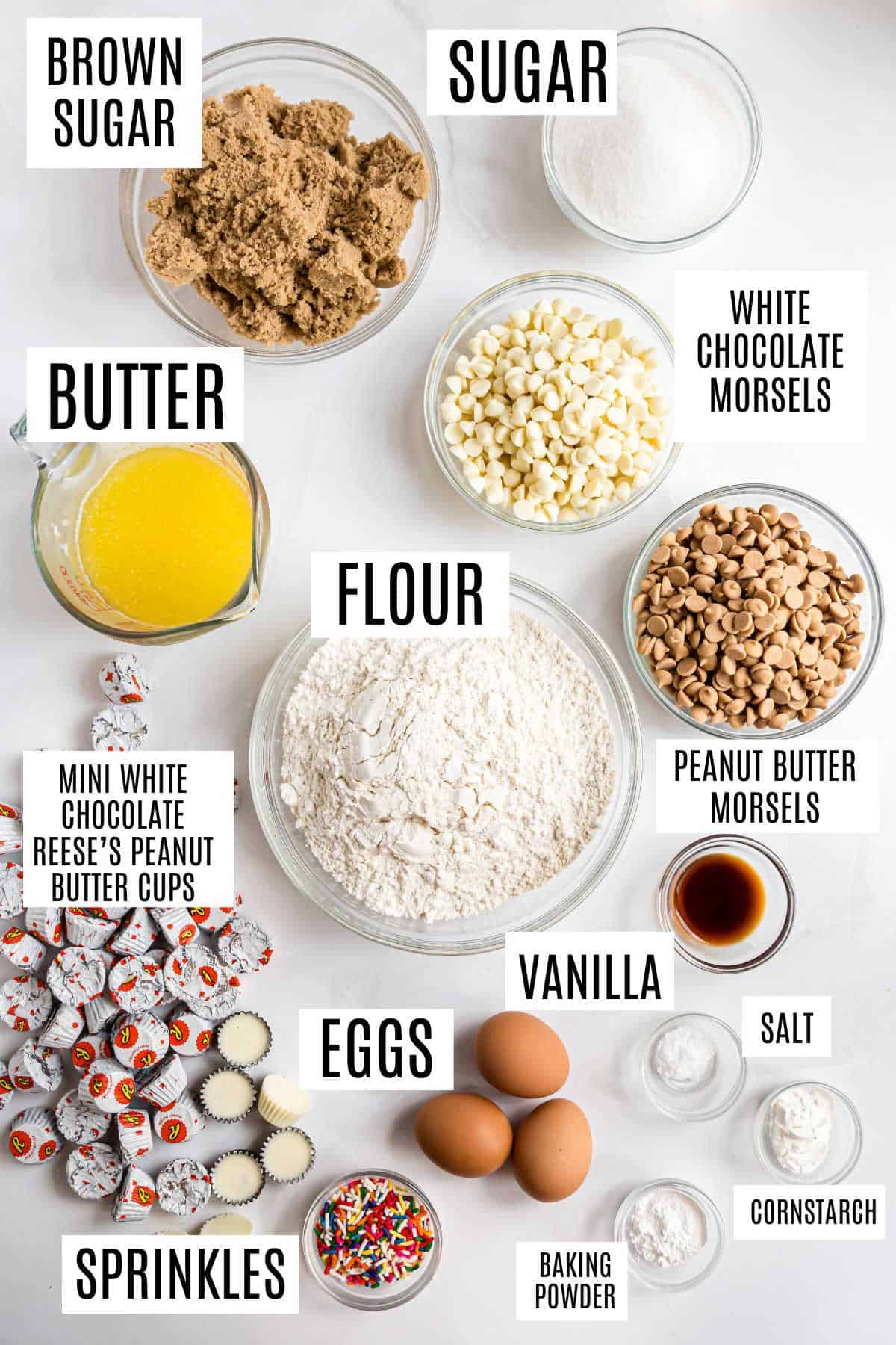 Baking ingredients on a counter, each labeled: sugars, butter, flour, eggs, chips, peanut butter cups, and sprinkles—perfect for making white chocolate peanut butter cookies.