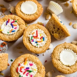 Mini cookie cups with white chocolate centers, frosting, and colorful sprinkles—these delightful treats are inspired by classic white chocolate peanut butter cookies. Perfect for any sweet occasion!.