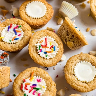 Mini cookie cups with white chocolate centers, frosting, and colorful sprinkles—these delightful treats are inspired by classic white chocolate peanut butter cookies. Perfect for any sweet occasion!.