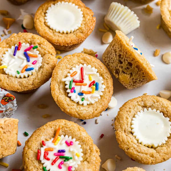Mini cookie cups with white chocolate centers, frosting, and colorful sprinkles—these delightful treats are inspired by classic white chocolate peanut butter cookies. Perfect for any sweet occasion!.
