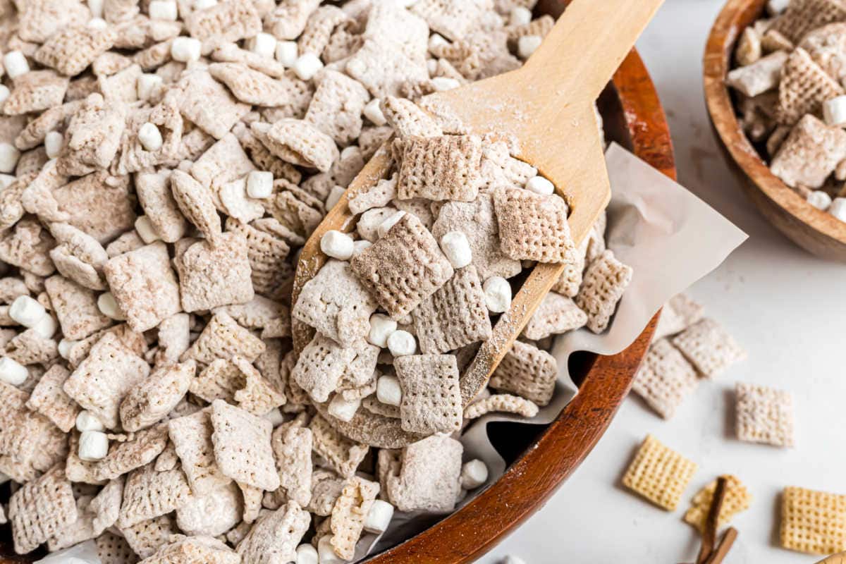 A wooden spoon scoops hot cocoa muddy buddies cereal with mini marshmallows from a bowl.
