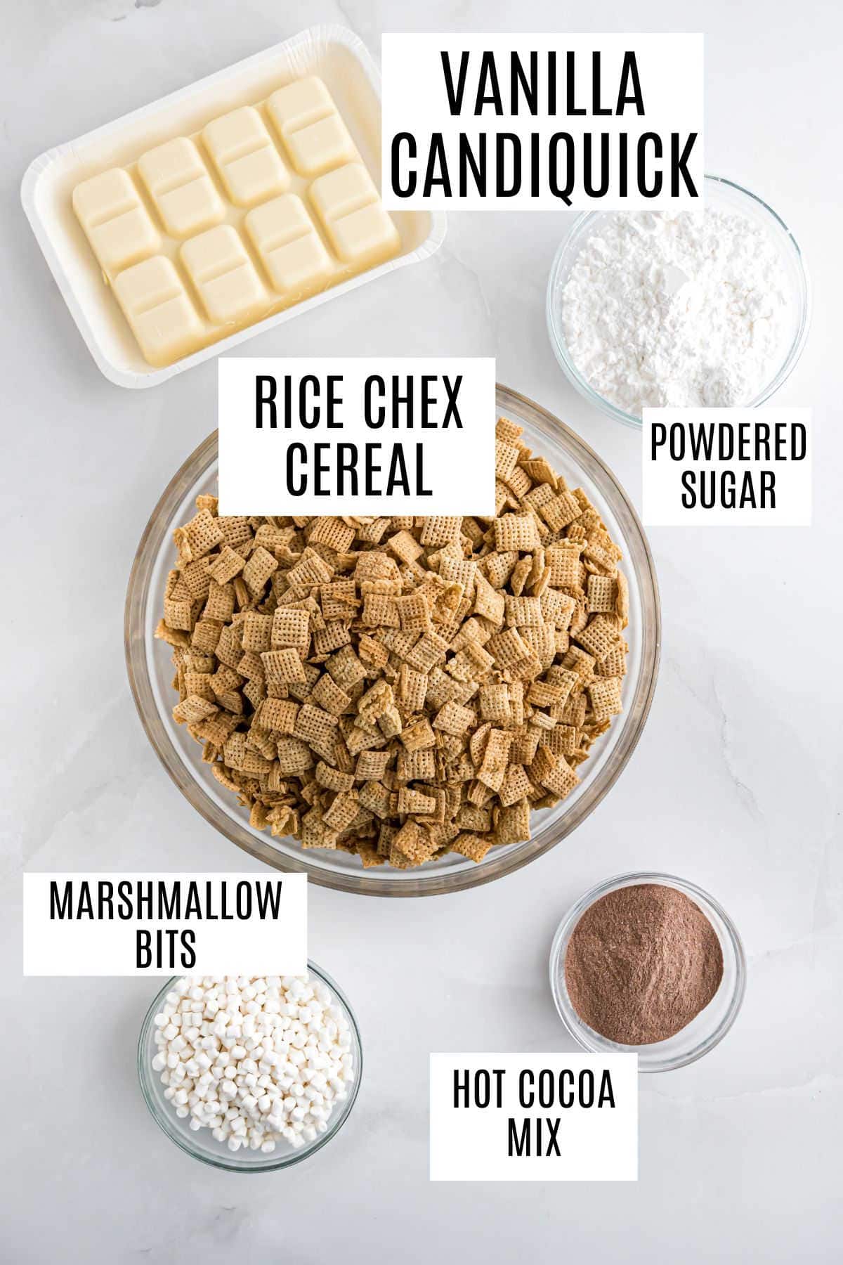 Bowls of Rice Chex cereal, marshmallow bits, powdered sugar, hot cocoa mix, and vanilla Candiquik are ready to make delicious hot cocoa muddy buddies on a white surface.