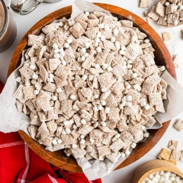 A wooden bowl filled with hot cocoa muddy buddies cereal, coated in powdered sugar and mini marshmallows.