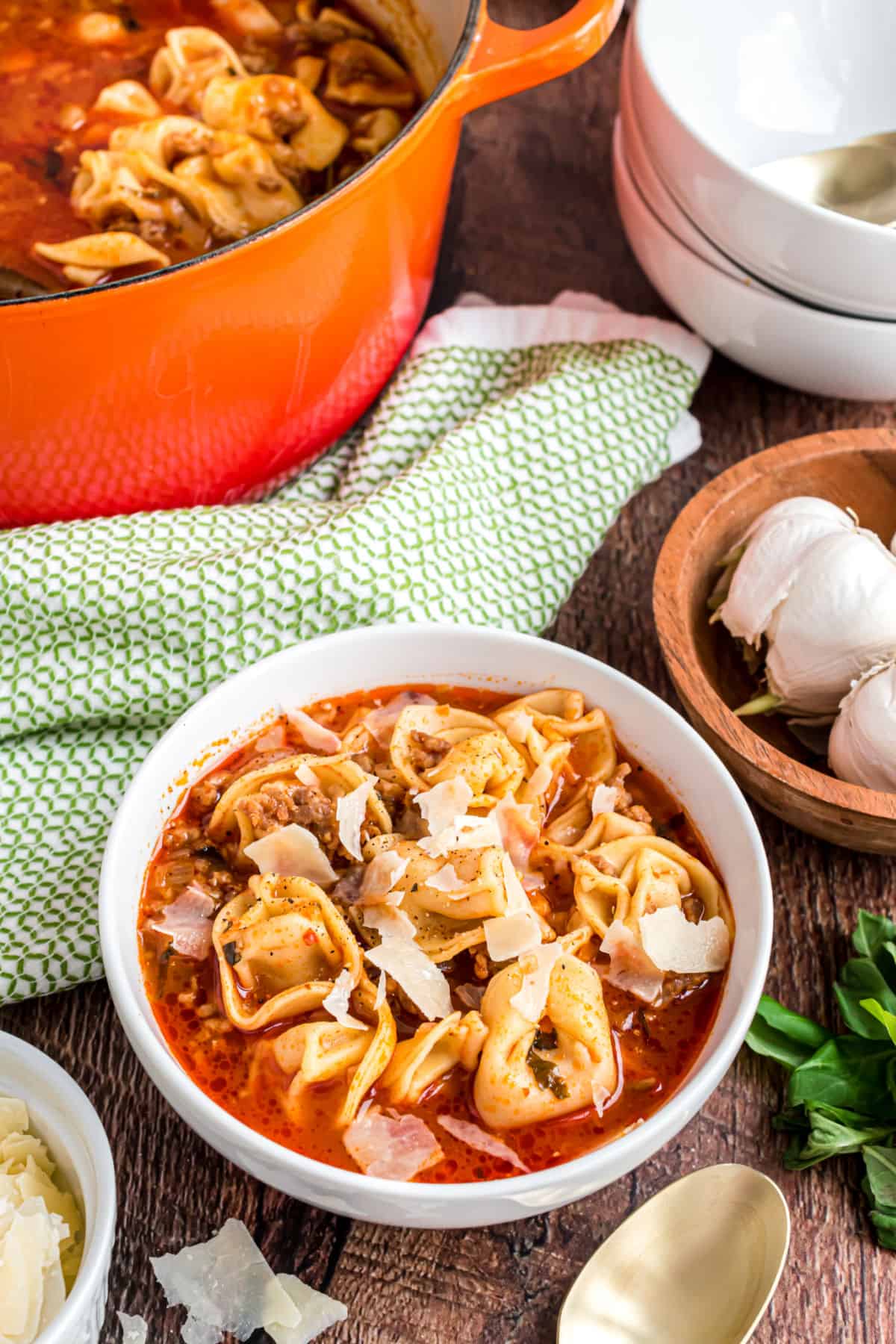 Sausage tortellini soup in a white bowl with shaved parmesan cheese.