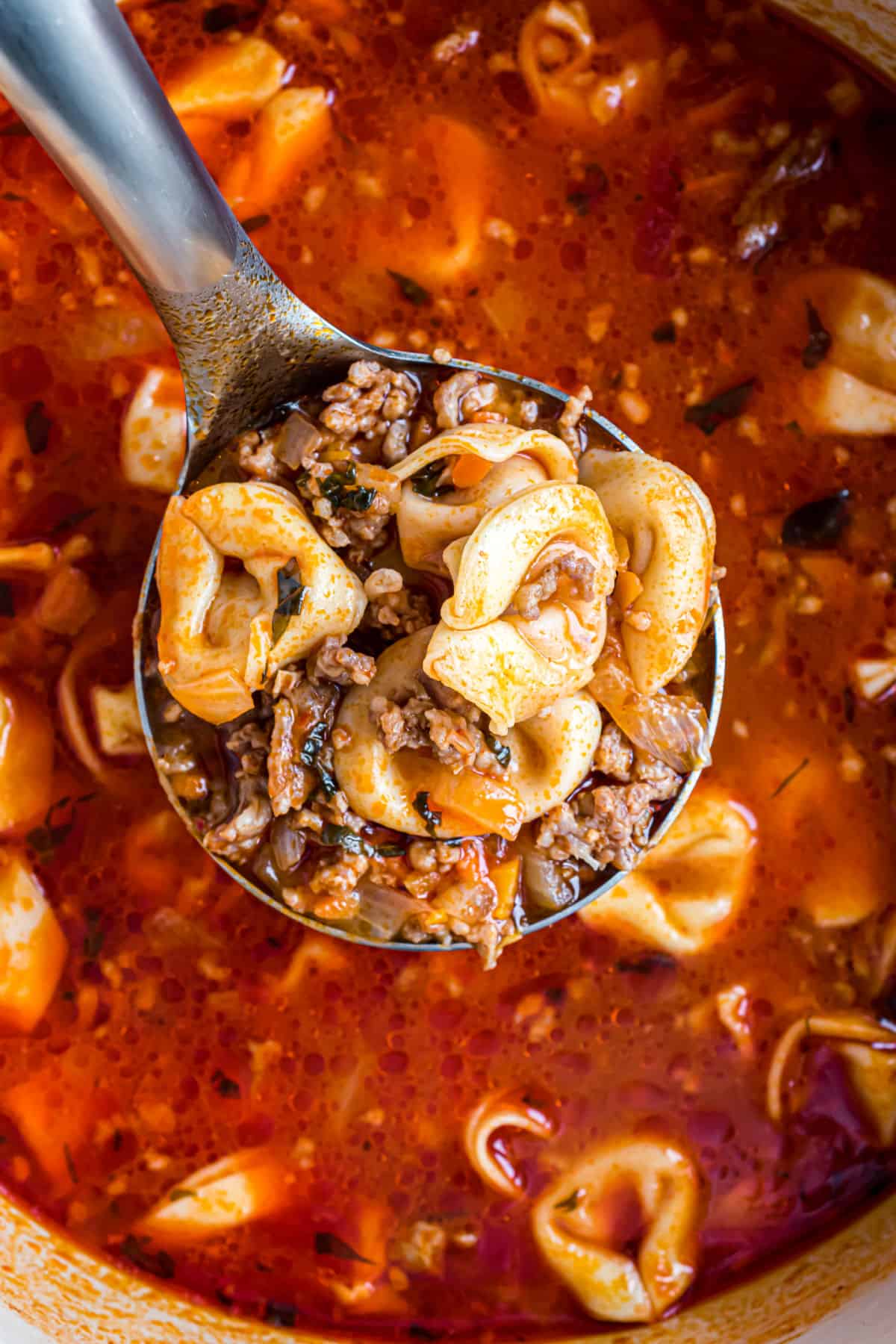 Sausage tortellini soup in a pot being scooped on a ladle.