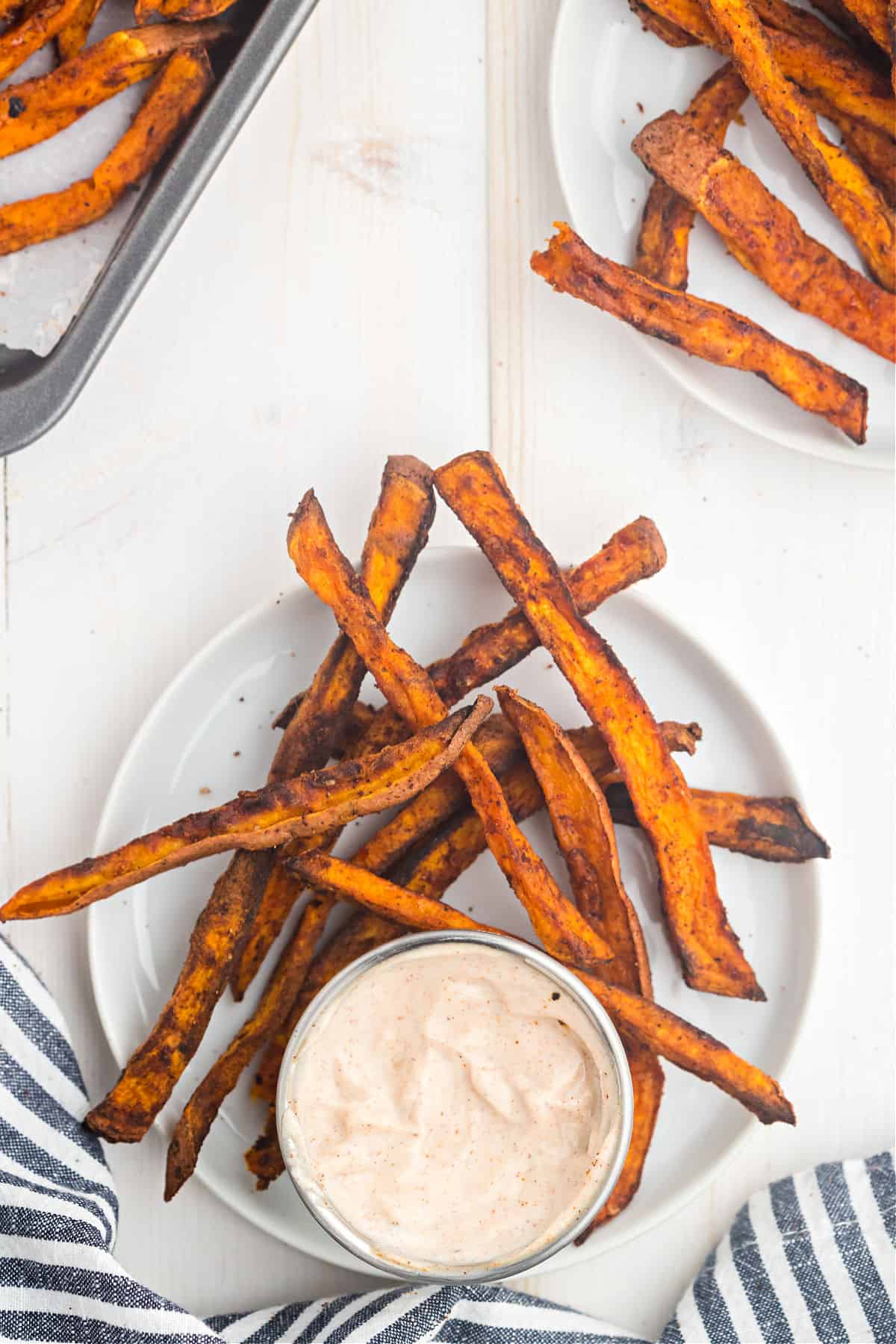 Sweet potato fries served on a white plate with a cup of cinnamon dipping sauce.