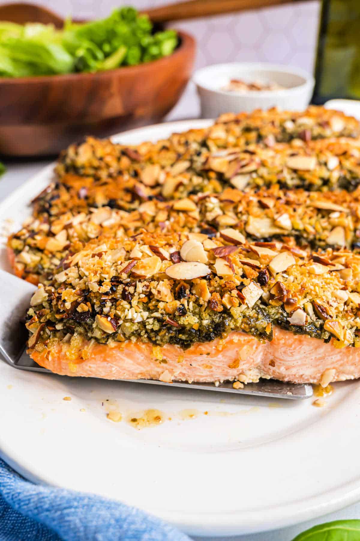 Baked almond pesto salmon fillet topped with a crispy herb crust, served on a white plate.
