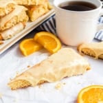 Orange scone with glaze on parchment paper.