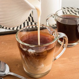 Coffee creamer being poured into a clear mug of coffee.