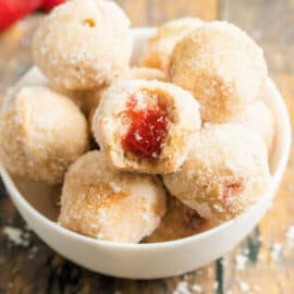 Jelly filled sugar coated donut holes in a white bowl.