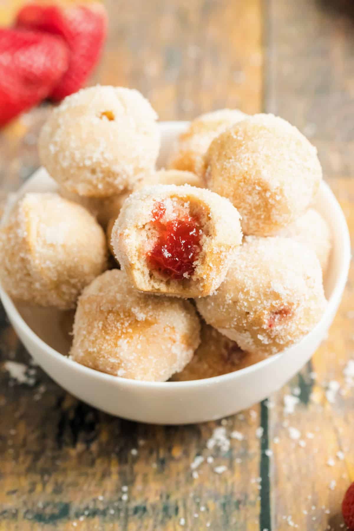 Jelly filled sugar coated donut holes in a white bowl.