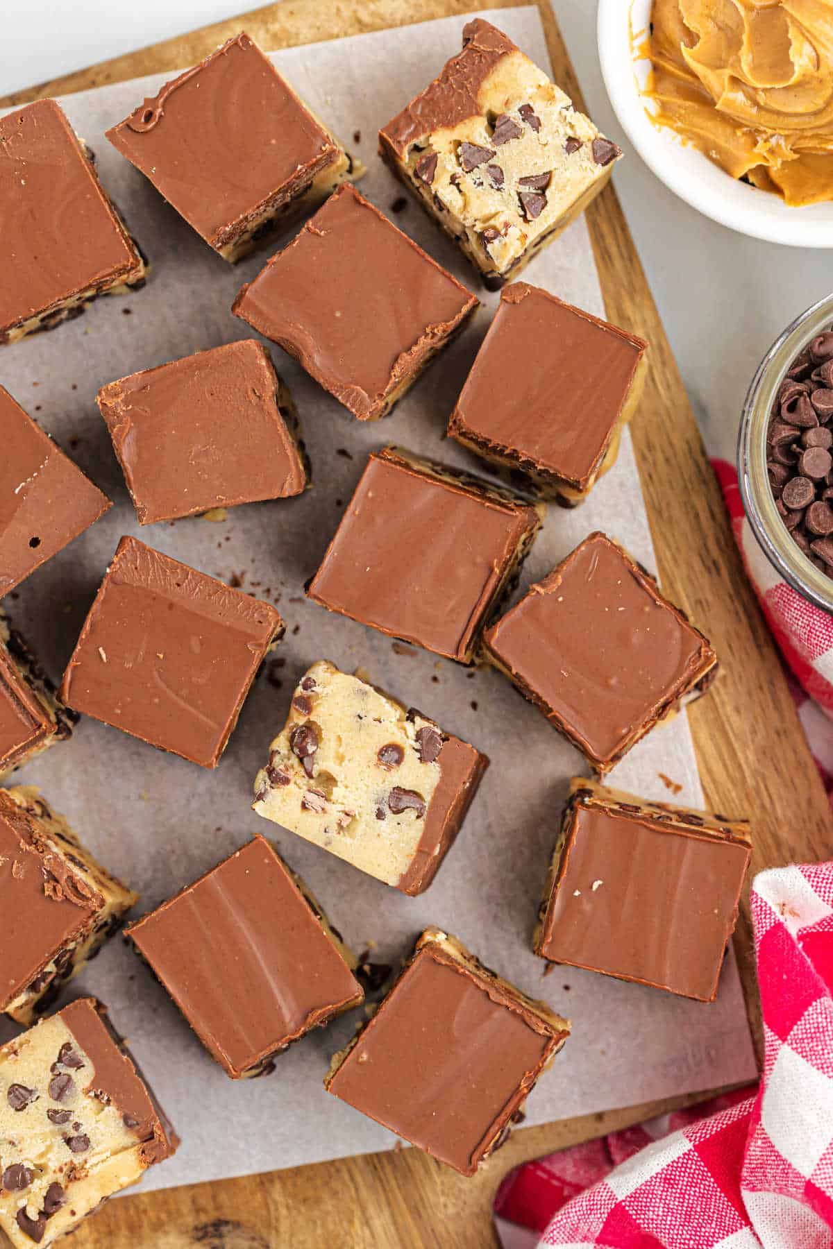 Pieces of cookie dough with fudge topping on a wooden cutting board.