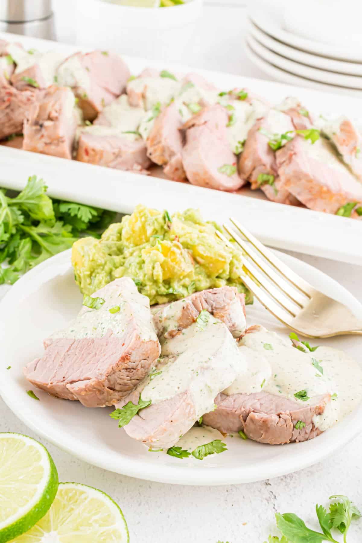 Slices of pork tenderloin with cilantro lime sauce on a white plate.