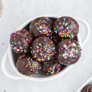 Oval white bowl filled with chocolate donut holes topped with sprinkles.