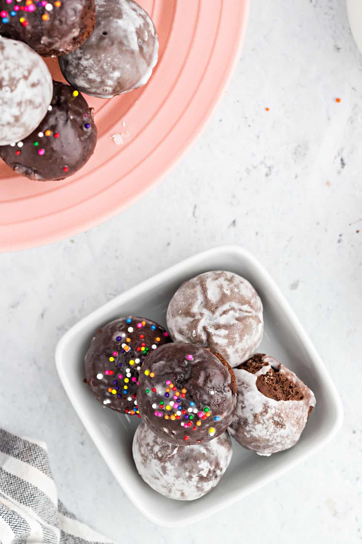 Glazed chocolate donut holes, some with sprinkles, in a white bowl.