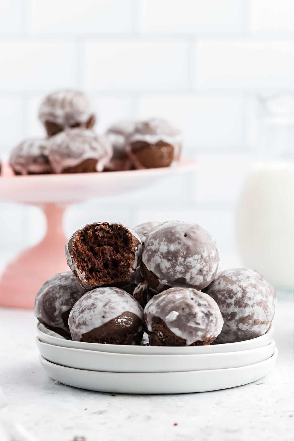 White stack of plates with glazed chocolate donut holes.