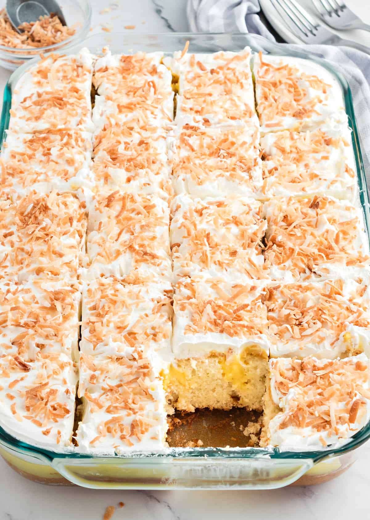 Coconut pudding cake cut into squares in a 13x9 dish.