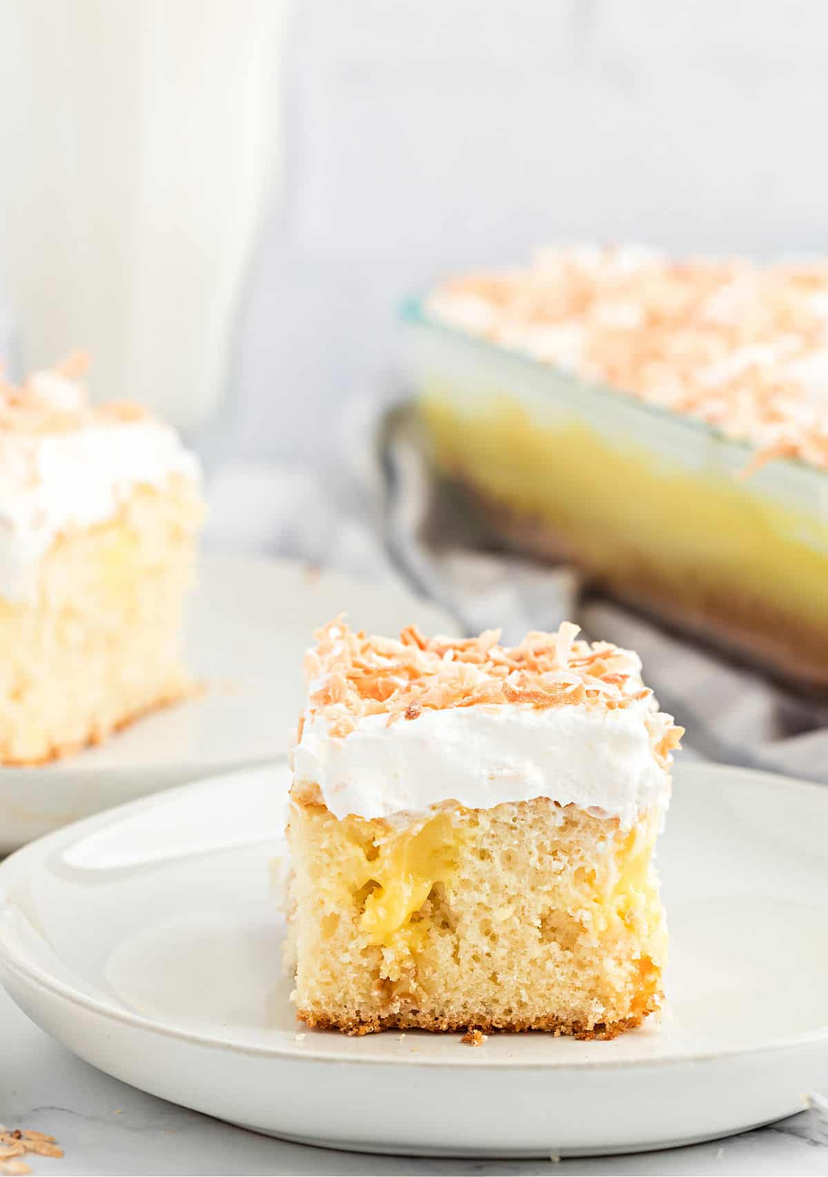 Slice of coconut cake with pudding and whipped cream on a plate.