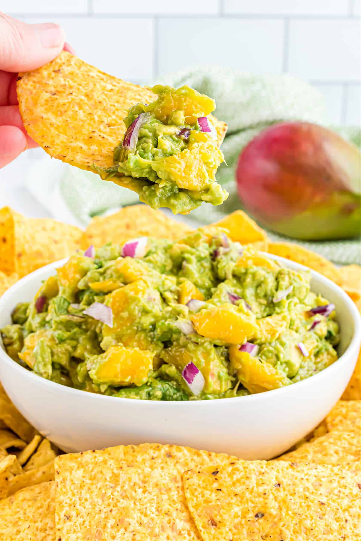 Mango guacamole in a white bowl scooped with a tortilla chip.