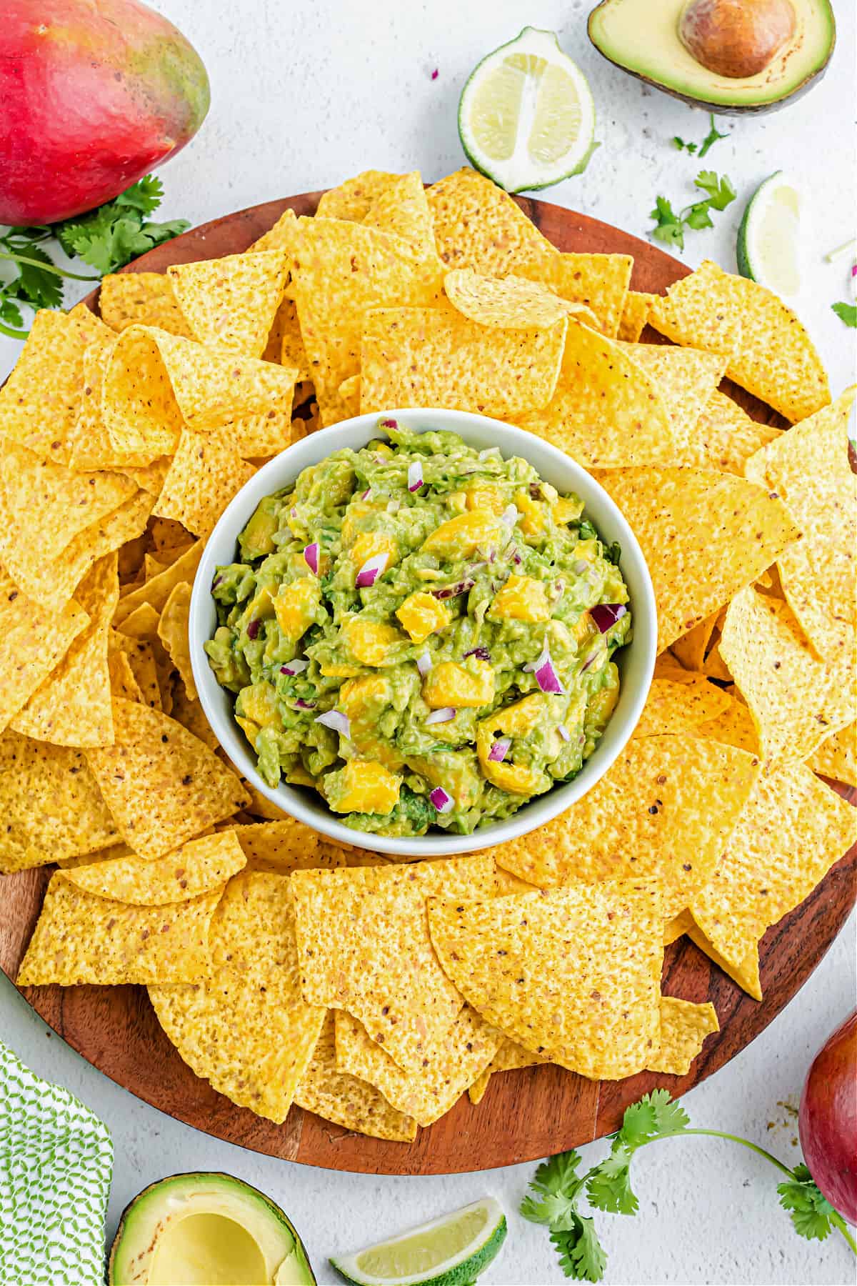 Guacamole with mangoes served in a bowl with a big platter of chips.