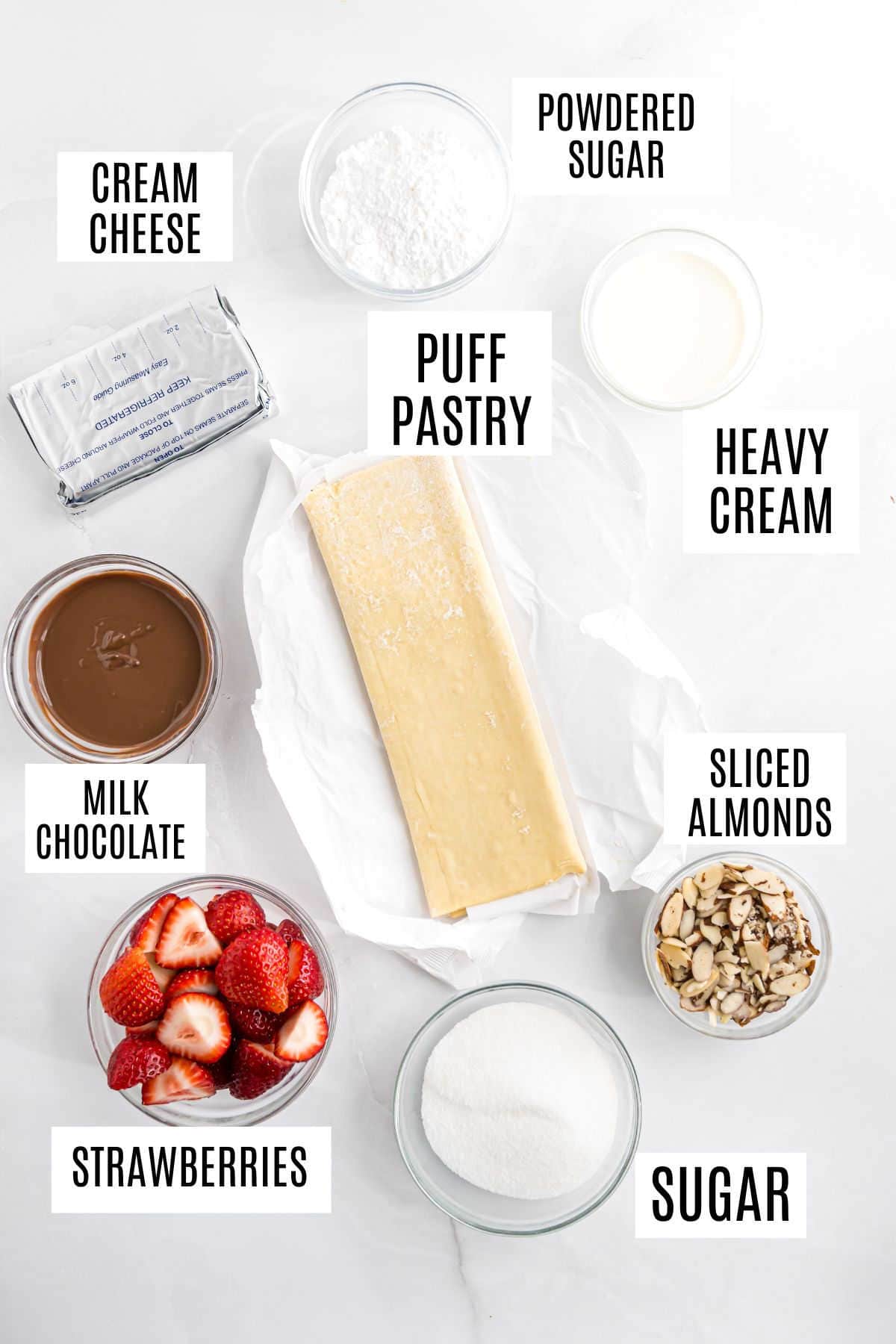 Ingredients for strawberry cheesecake napoleons: cream cheese, powdered sugar, puff pastry, heavy cream, milk chocolate, sliced almonds, strawberries, and sugar.