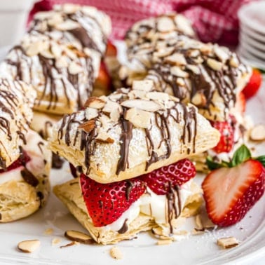 Strawberry cheesecake napoleons pastry with sliced strawberries, cream, chocolate drizzle, and almond slices, garnished with a strawberry half.