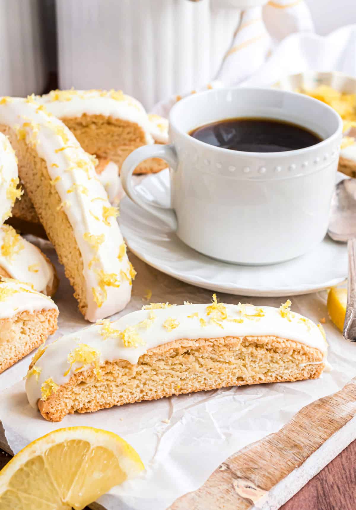 Lemon biscotti dipped in white chocolate served with a small white mug of coffee.