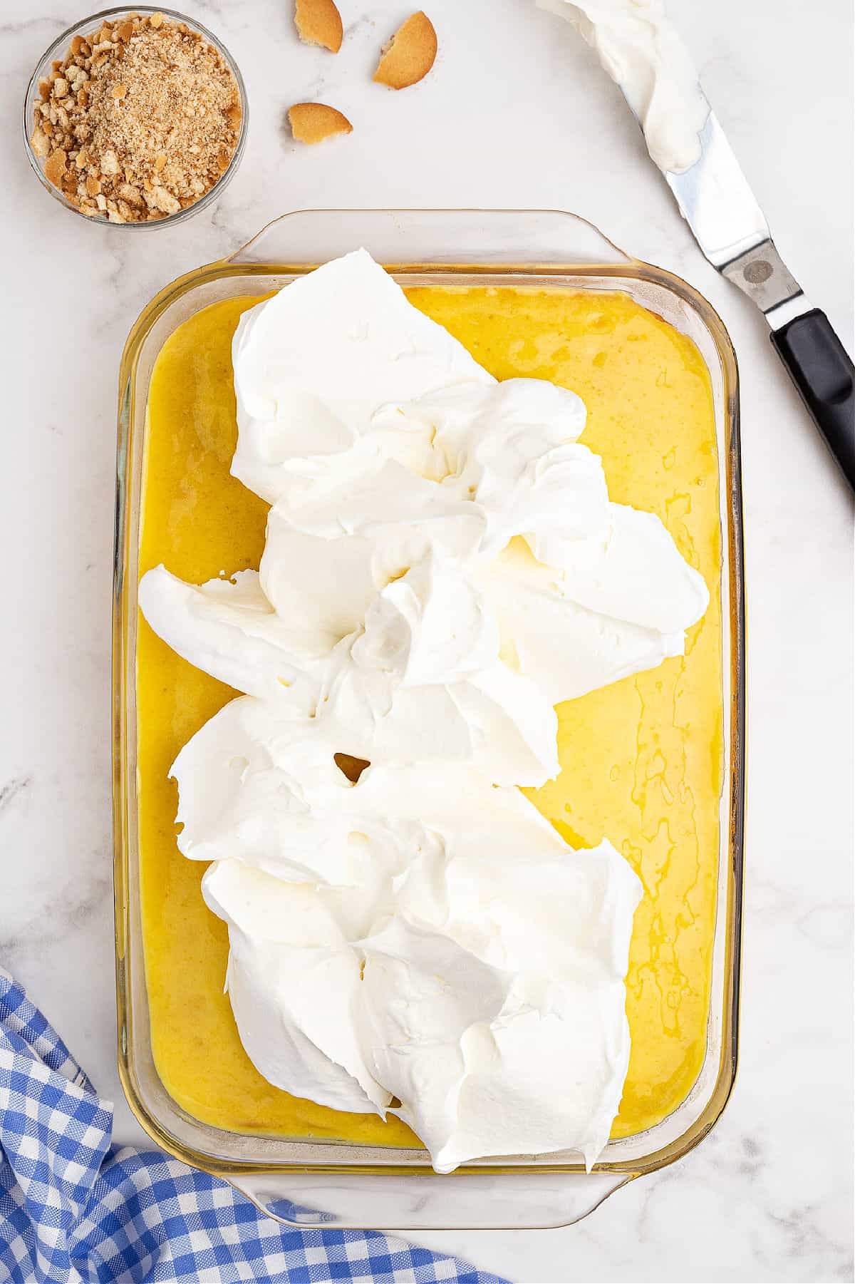 Whipped cream being spread over the top of a lemon poke cake.