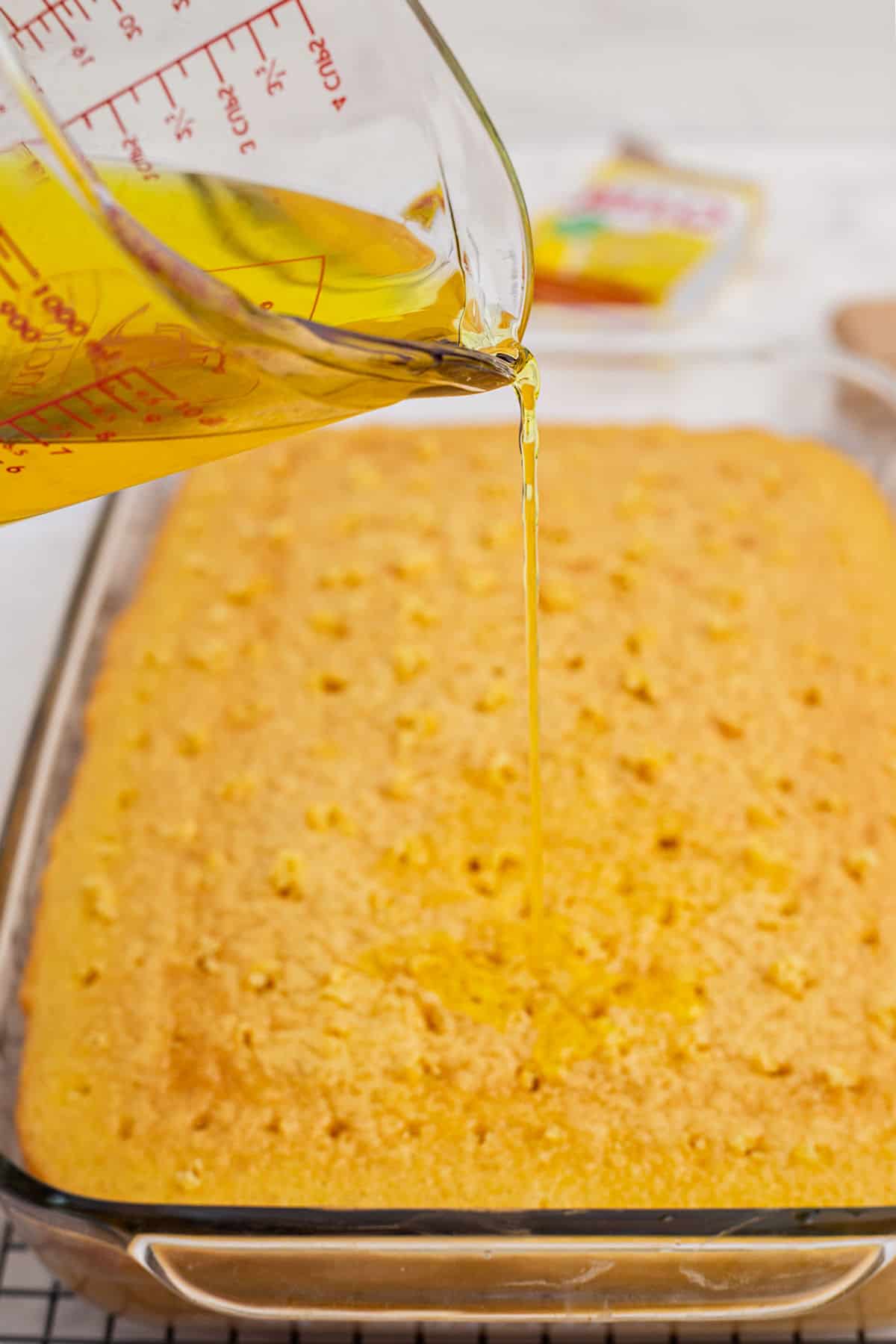 Lemon gelatin being poured over a baked cake.