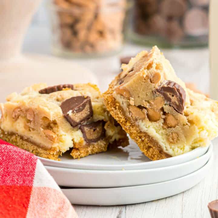 Peanut butter cheesecake bars served on a stack of white plates.