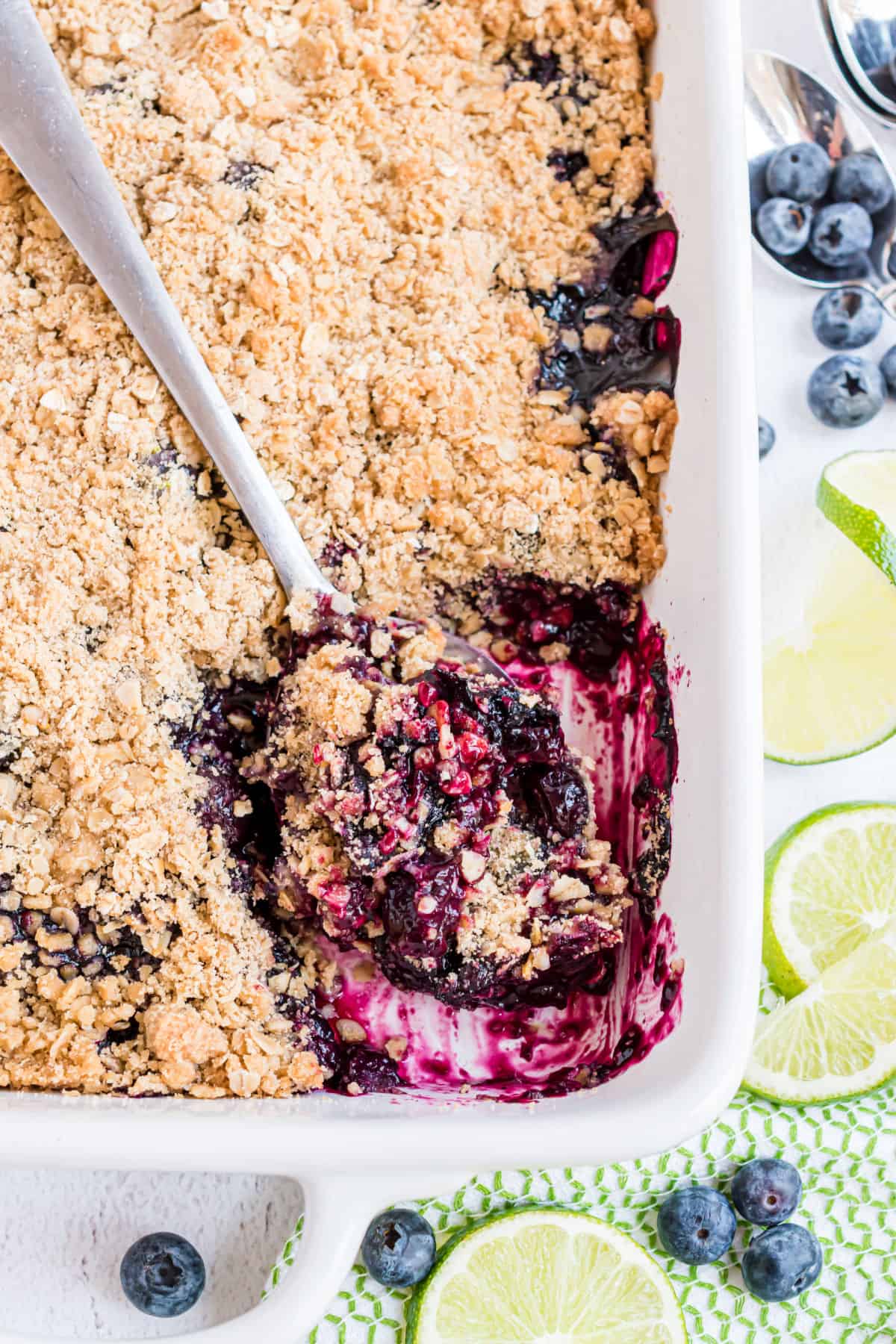 Blueberry crumble baked in a white dish with a spoon scooping it out.