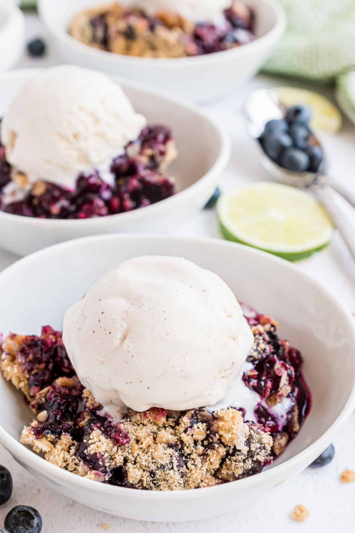 Blueberry crumble served in white bowls and topped with vanilla ice cream scoops.