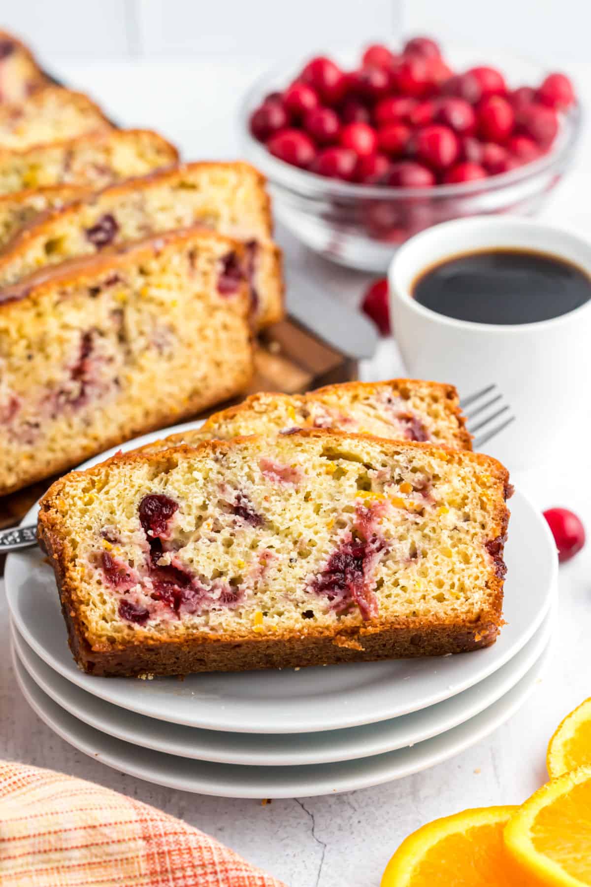 Two slices of cranberry orange bread on a stack of white plates.