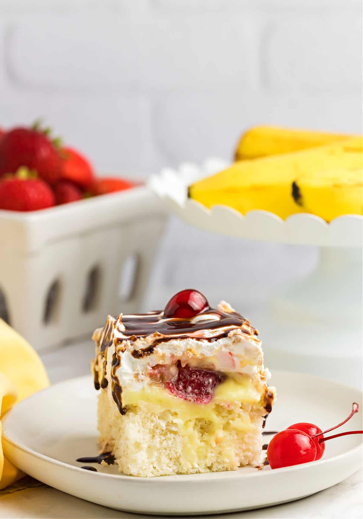 Slice of cake with bananas, strawberries, and pineapple on a white plate.