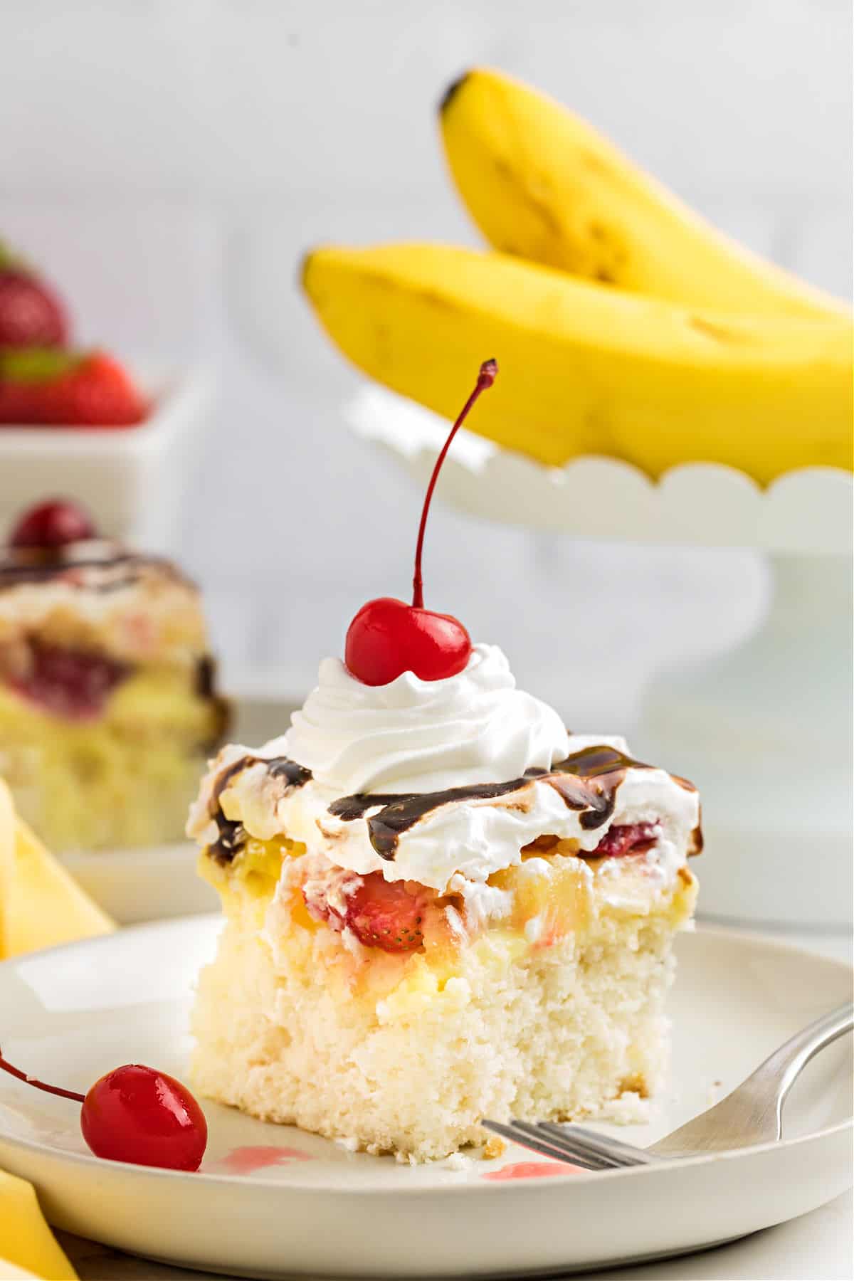 Slice of banana split poke cake on a white dessert plate.